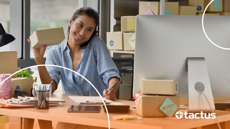 Pequena empresária sorrindo ao lado de caixas e do seu computador, feliz por ter uma boa contabilidade para e-commerce