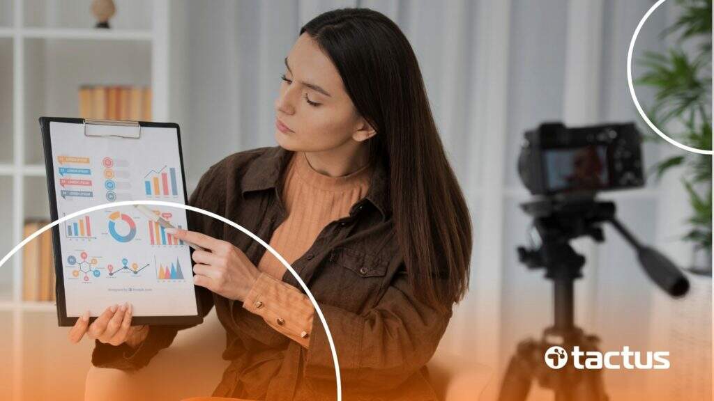 Imagem mostra mulher, à frente de uma câmera, apontando para gráficos em um tablet, para simular como declarar ganhos com youtube no imposto de renda