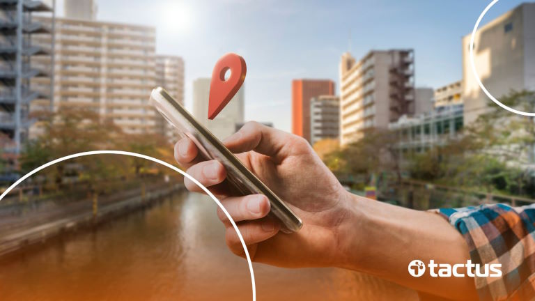 Imagem mostra mão com celular à frente de grandes edifícios comerciais, para demonstrar como funciona a sede virtual para MEI